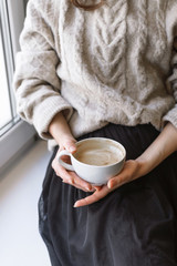 Closeup of woman's hand holding cup with latte in front of the window, shallow selective focus