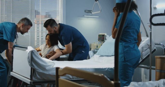 Male nurse and doctor lifting patient into his bed
