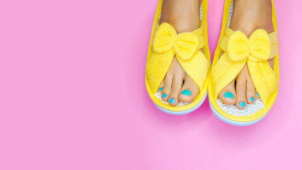 Spa day - perfect holiday for yourself concept.  Bare feet with pedicure and wearing yellow funny slippers over pink background