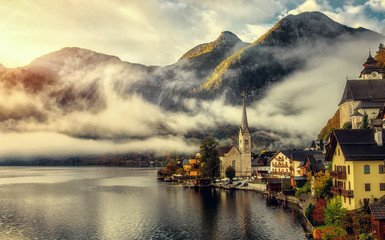 Fototapeta premium Impressive athmospheric scene. view on Hallstatt Lutheran Church, with Morning Fog under sunlit at sunrise. Hallstatter, Salzkammergut, Austria. traditional picture-postcard for tourist destination