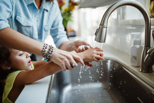 Mother and daughter washing hands in kitchen sink at home