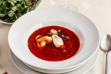 Delicious tomato clam chowder soup with shellfish, shrimps, squid, mussels, octopus and seafood close-up on a in a white bowl on the  on a served white table