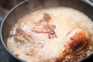 Cooking fried chicken in a black frying pan in sunflower oil with crusty steam in a steam boiling at high temperature
