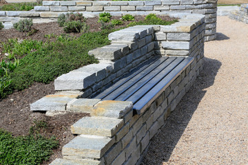 Moderner Garten- und Landschaftsbau: Mauer aus Natursteinen mit integrierter Sitzbank und Anpflanzungen entlang eines Gehwegs