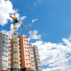 Fototapeta na wymiar Tower crane building new modern apartment house on a background of blue cloudy sky at sunny day. Real estate concept.