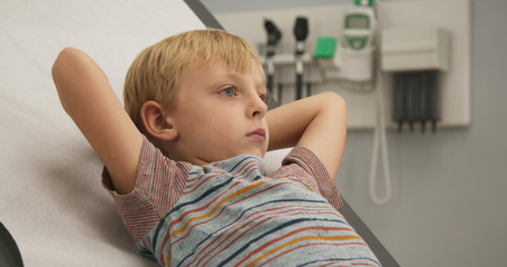 Close up of Little boy waiting on exam table in doctor's office. Young Caucasian child going to pediatrician for regular visit