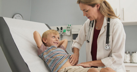 Fototapeta premium Female pediatrician performing regular check up on young boy in clinic exam room. Woman doctor giving exam to child in pediatrician office