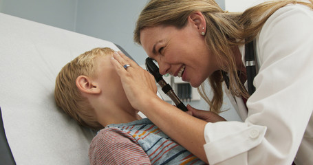 Close up of little boy getting eye exam at pediatrician office from female doctor. Woman physician using ophthalmoscope to look into eyes of a child