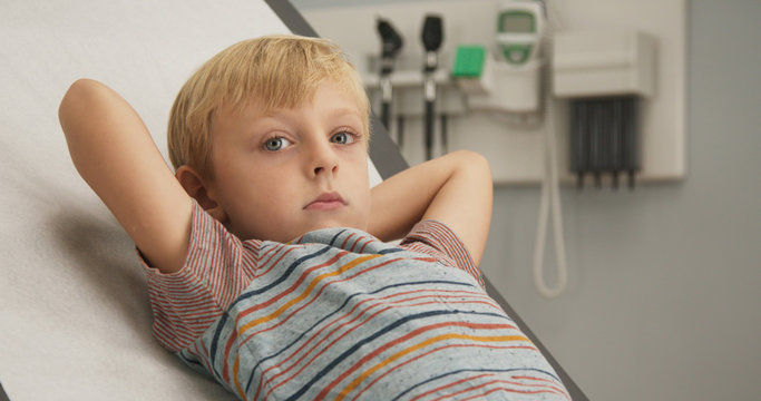 Close up of Young Caucasian child going to pediatrician for regular visit. Little boy waiting on exam table in doctor's office