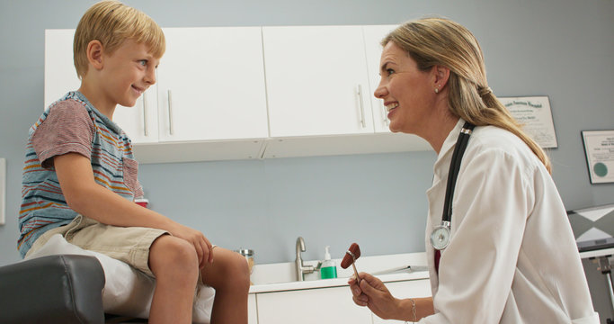 Little boy at pediatric office checking his reflexes with hammer while doctor watches. Female pediatrician showing patient how reflex hammer works