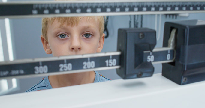 Close up of little boy being weighed on scale at pediatrician. Child patient visiting doctor for regular check up