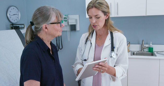 Female doctor showing test results on tablet computer to senior Caucasian patient. Woman visiting primary care physician for regular check up