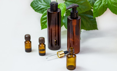 Dark cosmetic bottles and green natural leaves on a light background. Copy space Beauty salon blogger, salon therapy, minimalist concept. The concept of natural environmentally friendly cosmetics.