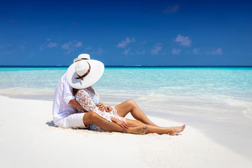 Fototapeta na wymiar Verliebtes Paar in weißer Sommerkleidung sitzt am tropischen Strand und genießt den Urlaub 