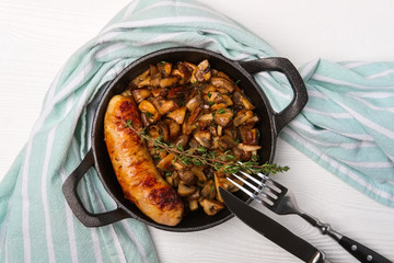 Cast-iron pan with fried sausage and mushrooms, flat lay, top view.