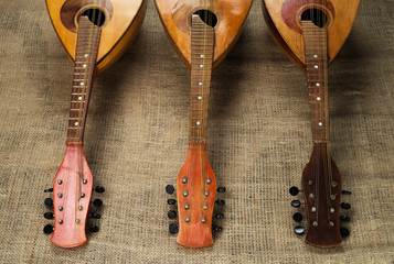 Three old mandolins rotated fingerboards to the camera on a background of rough burlap texture.