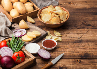 Fresh organic homemade potato crisps chips in wooden bowl with sour cream and red onions and spices on wooden table background. Fresh yellow potatoes with ketchup