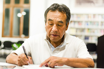 Serious senior man sitting on a library bench writing in his book. Senior man sitting in a...