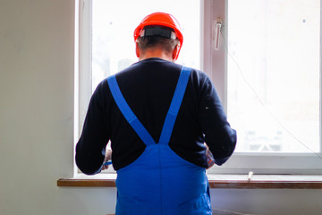 A builder in an orange construction cup in his hands with a spatula and a white putty. Blue form...