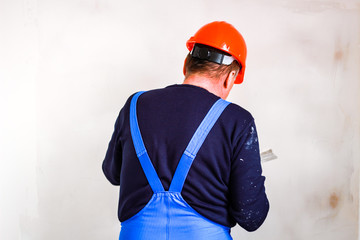 A builder in an orange construction cup in his hands with a spatula and a white putty. Blue form...