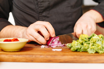 Chef cuts onion. Wooden. Arugula. Ingridients. Cooking. Raw.