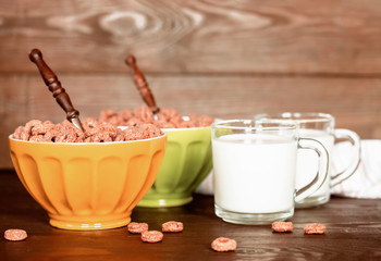 corn chocolate rings in bowls on the table and cups of milk for breakfast. ready-made snacks of corn flakes on the kitchen table close-up.