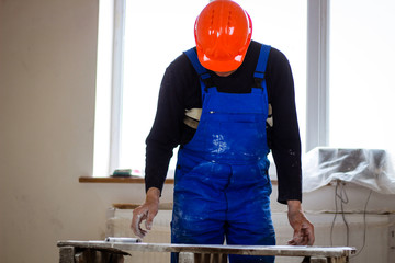 A builder in an orange construction catcher in his hands with drawings. Blue form combining. Repair...