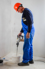 A builder with a construction helmet in his hands with a dribble. A uniform form of combinzon. Repair in the apartment