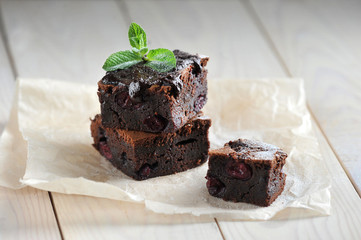 Chocolate brownie with cherry. Pieces of brownie laid out on paper. Shiny wooden background....