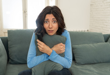 Portrait of a young woman looking scared and shocked watching scary movie on TV.