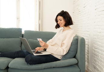 Obraz premium Happy young woman sitting with laptop and a credit card shopping online at home