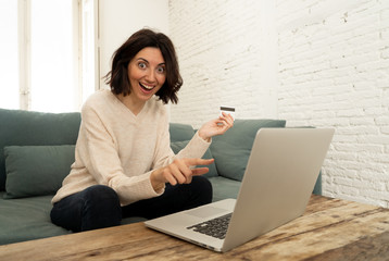 Happy young woman sitting with laptop and a credit card shopping online at home