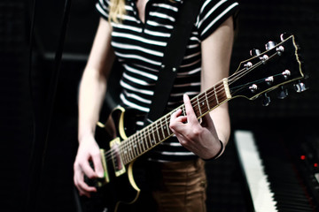 Fototapeta na wymiar A girl in a striped shirt with an electric guitar stands on the recording Studio. The guitarist plays the strings of a musical instrument. Acoustic background with soundproofing
