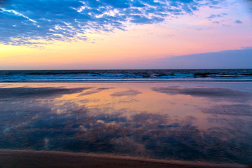 Fototapeta na wymiar The beautiful soft pinks and blues of early sunrise at the beach are reflected on ripples in the water at low tide.