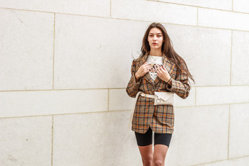 Portrait shooting of a stylish girl. Beige shades. Trends of spring and summer 2019. Wide jacket and belt leather bag. White sneakers and bike shorts