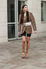 Obraz premium Portrait shooting of a stylish girl. Beige shades. Trends of spring and summer 2019. Bike shorts. Thick cloak, cover jacket. Gold earrings. Heels