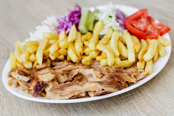 Chiken Doner Kebab on the plate with french fries, tomatoes, onion, pickles and salad on a wooden background. Grilled chicken meat with vegetables.
