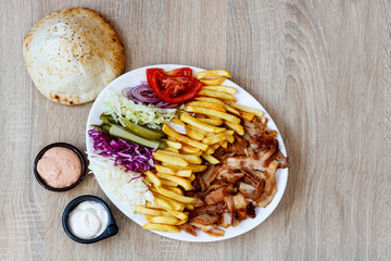Chiken Doner Kebab on the plate with bread, french fries, tomatoes, onion, pickles and salad on a wooden background. Grilled chicken meat with vegetables.