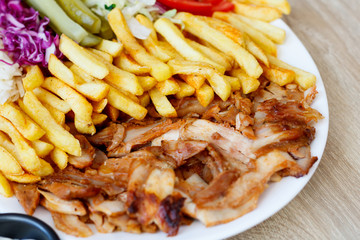 Chiken Doner Kebab on the plate with french fries, tomatoes, onion, pickles and salad on a wooden background. Grilled chicken meat with vegetables.