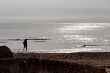 Silhouette of a woman collecting mussels on a Senigallia beach against a shimmering Adriatic Sea...