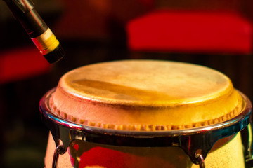 Obraz premium Traditional ethnic Cuban conga drum on red background. Musical instrument made of wood covered with leather and microphone. Ethnic drum set at a concert of jazz music.