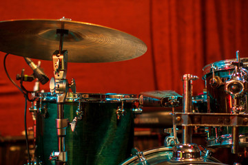 Fototapeta na wymiar Green drum set on red background. Percussion instruments at a jazz concert. Drum and plates are on the stage of the concert hall