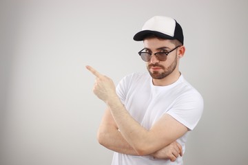 young man casually dressed wearing sunglasses pointing him to the side and looking at the camera - whit space for caption or text