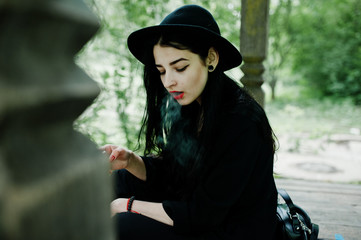 Sensual smoker girl all in black, red lips and hat. Goth dramatic woman smoking thin cigarette.