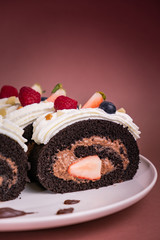 Chocolate roll cake with berries and fresh cream on brown background.