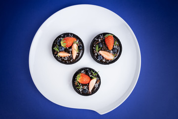 Cookie crust chocolate tart with Blueberry and strawberry set on Blue Background.