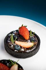 Cookie crust chocolate tart with Blueberry and strawberry set on Blue Background.
