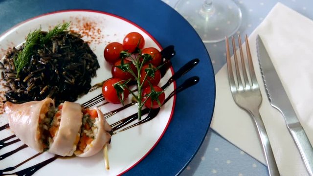 Image of stuffed squid with wild rice and cherry tomato on the plate indoors