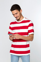 Handsome young man texting on mobile phone with red white tshirt and blue jeans on white background