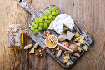 Different cheeses, walnuts, honey and green grapes on a wooden table, a view from the top.